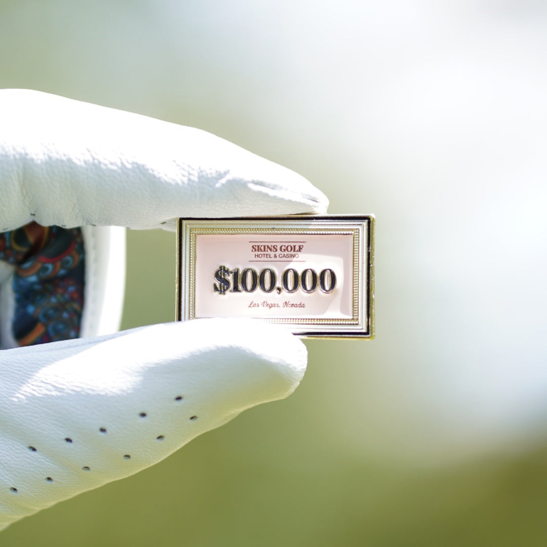 $100,000 ball marker plaque held by a white glove against a light green background