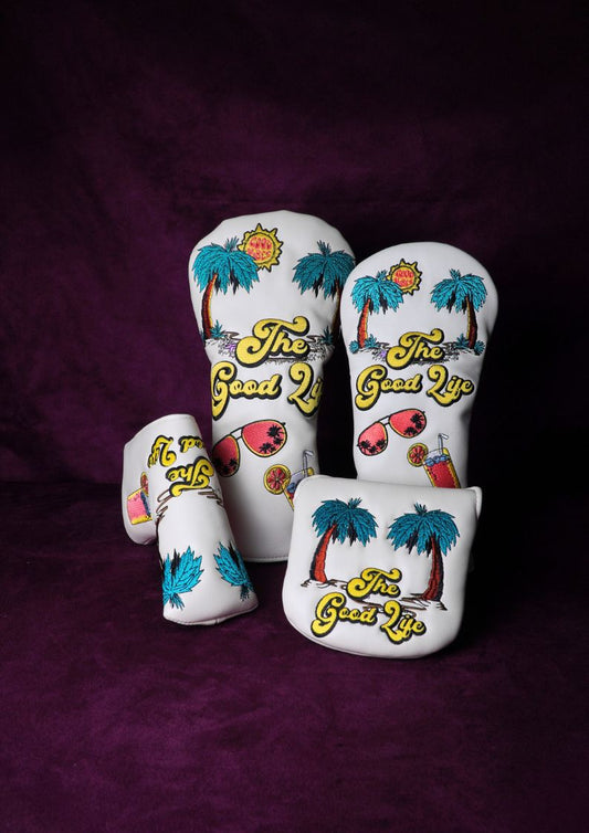 Three white golf club head covers with 'The Good Life' design on a purple background