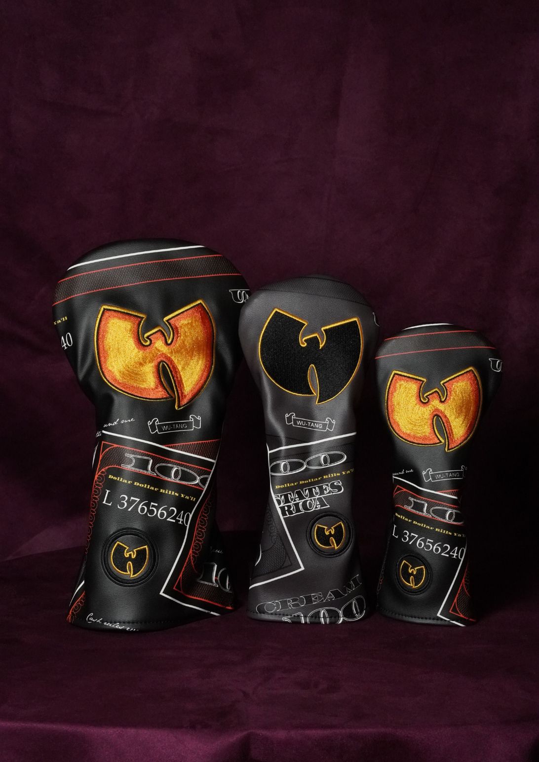 Three custom golf club headcovers featuring a black background with a large gold and orange Wu-Tang Clan logo and white text, displayed on a dark purple fabric background.