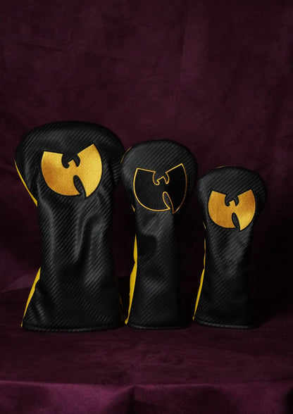 Three black carbon-fiber-textured golf club headcover sleeves with gold Wu-Tang Clan logo designs, arranged in descending size order on a dark purple fabric background.