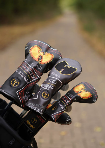 Three golf club headcovers with a black and gold Wu-Tang Clan design, resting in a black golf bag on a blurred path.