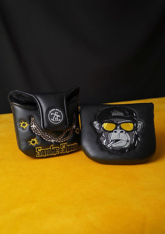 Two black leather golf putter headcovers on a yellow surface with a dark background