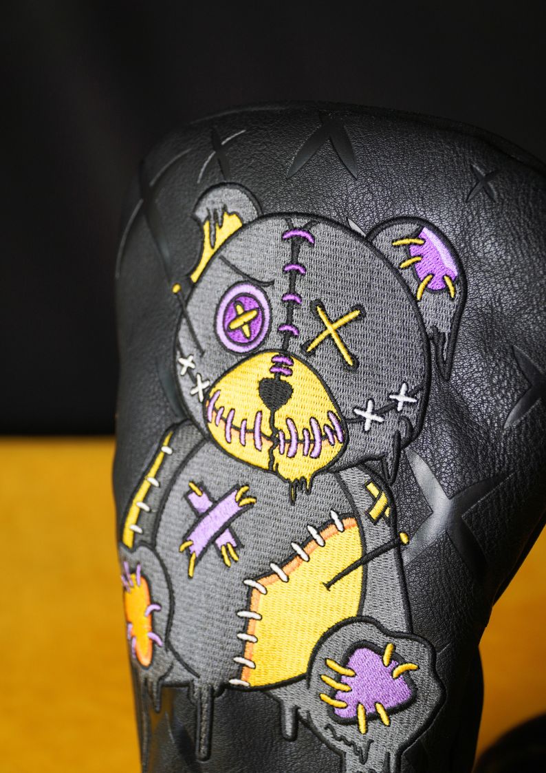 Voodoo bear with yellow and purple accents on golf headcover on a black background