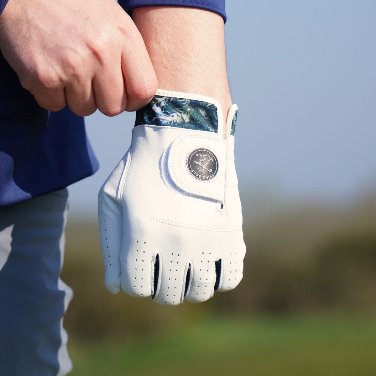 White golf glove held by a person on a blurred outdoor background