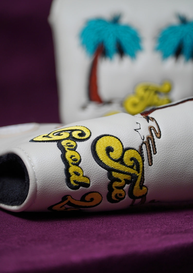 Close-up of a white golf headcover with colorful text and graphics on a purple background.