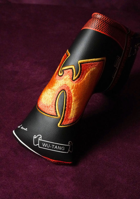 A black leather golf headcover with a large orange and yellow flame design on the side, resting on a dark purple textured background. The headcover features the brand name 'WU-TANG' printed on the lower front.