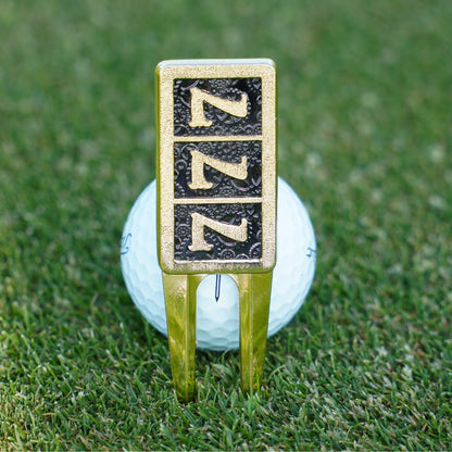 Golf ball with a gold and black divot tool on a grassy background