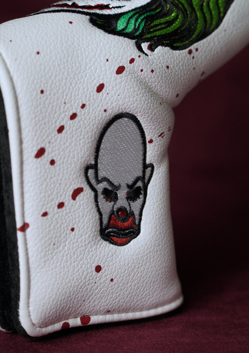 Close-up of a white golf headcover with a Joker design and red specks on a dark background