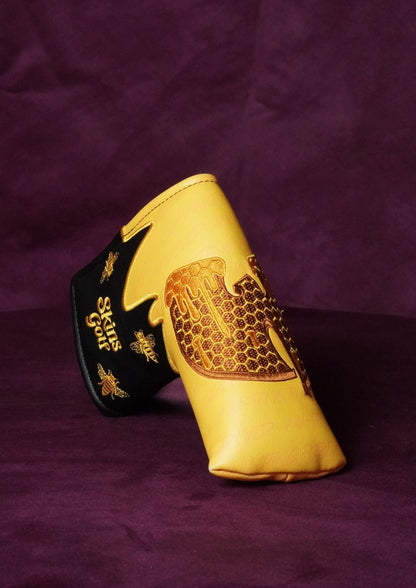 A blade headcover for golf in a yellow and black colorway, decorated with gold embroidered bee and floral patterns, displayed on a dark purple fabric background.