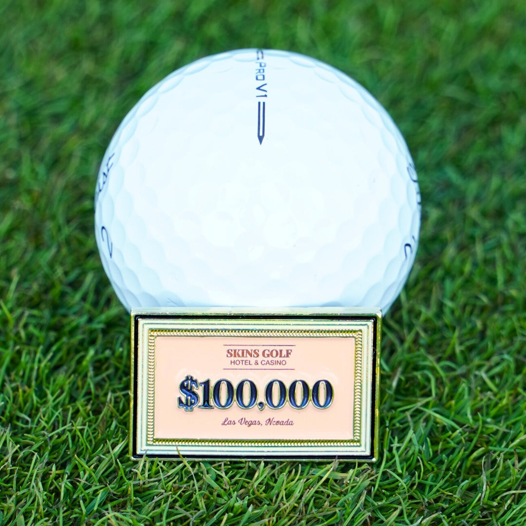 Golf ball marker with a $100,000 skins golf design on grass