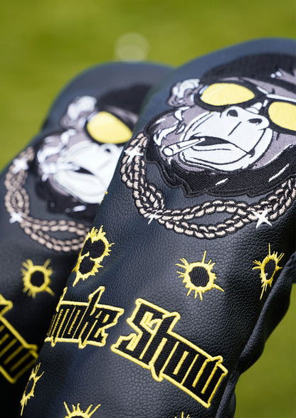 Black golf headcovers with graphic designs and text on a grassy background
